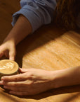 Person holding Pirch espresso glass with latte art on wooden table in sunlight